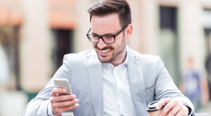Guia de Google Discover 2022: Webshare ajuda você Homem de óculos e terno sorrindo e olhando para o celular.