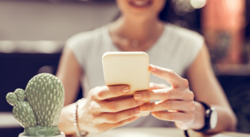 Guia de Google Discover 2022: Webshare ajuda você Mulher desfocada ao fundo olhando para o celular que está ofocado à frente da imagem.
