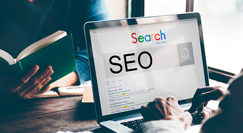 SEO Mitos e Verdades: O host do domínio faz diferença para SEO? Notebook aberta e na tela , a palavra SEO em uma página de algum buscador simulando o Google