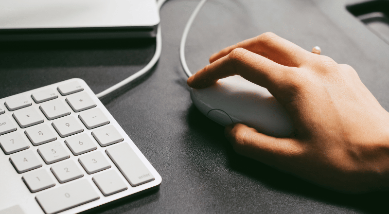 Como criar um logo para minha empresa? Guia completo com todas as etapas que você deve seguir Mão segurando mouse branco e aparece tb um pouco do teclado branco também.