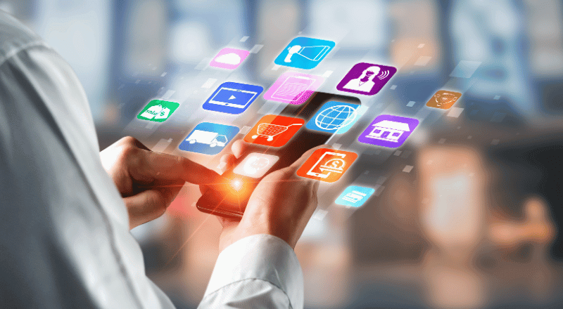 Estratégias de SEO: conquiste o topo das buscas Mulher segurando um celular e de dentro deste dispositivo está saindo u diversos ícones tecnológicos translúcidos, indicando que ela está estudando estratégias de SEO.