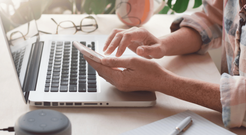 Busca orgânica: o que é e como se destacar no Google Pessoa digitando em celular em frente a um notebook.
