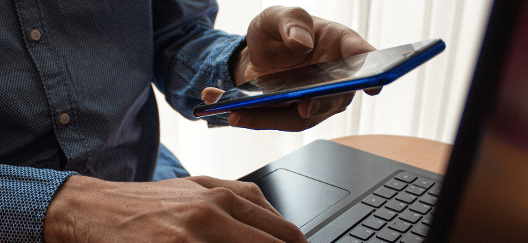 Homem mexendo no notebook e no celular ao mesmo tempo