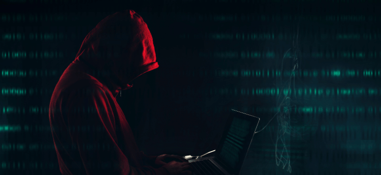 Homem de moletom com capuz vermelho em um ambiente escuro, tecla em um notebook, Simbolizando o uso de cloaking SEO.