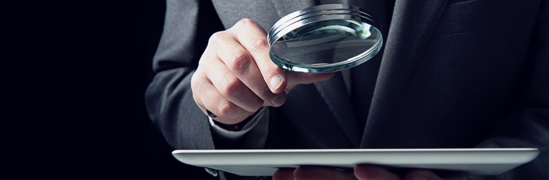 Homem segura uma lupa sobre um tablet.