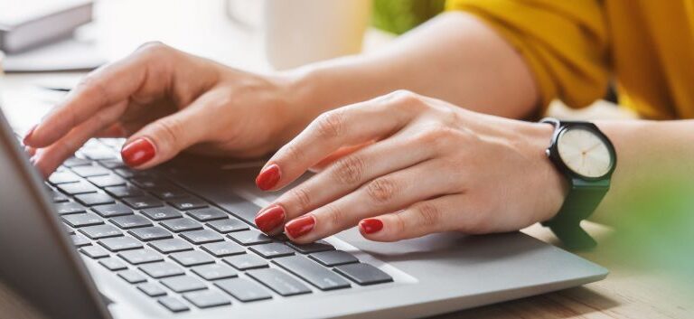 mãos com unhas pintadas de vermelho digitando em um notebook