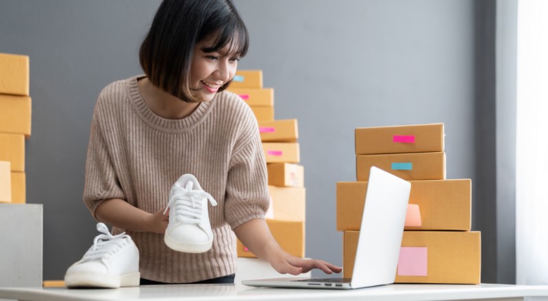 Mulher com um tênis na mão e mexendo no notebook